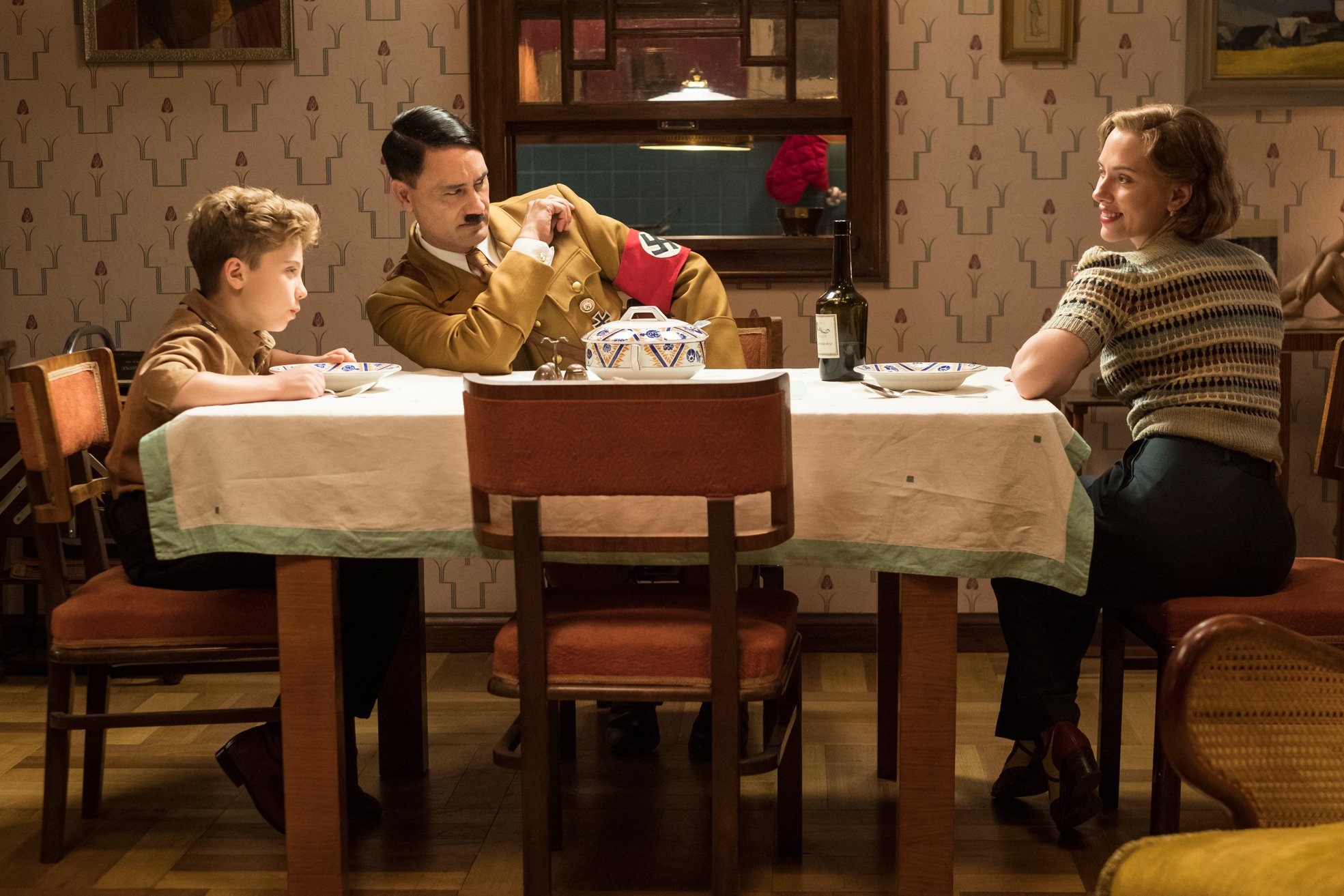  Jojo (played by Roman Griffin Davis) having dinner with his imaginary friend Adolf (played by writer/director Taika Waititi), and his mother, Rosie (Scarlett Johansson)
